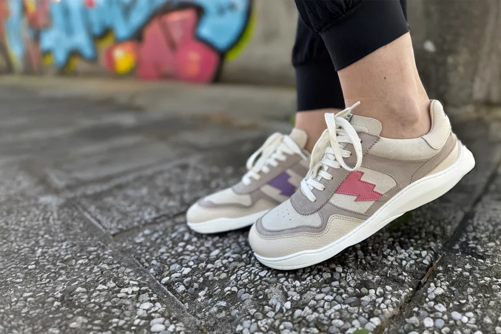 Side view of Dolfie Paradise Supersonic barefoot sneakers with lightning bolt design, worn on feet near colorful graffiti wall