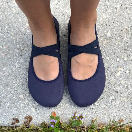 Top view of Clotsy navy barefoot ballet flats with elastic cross straps, worn on feet standing on pavement